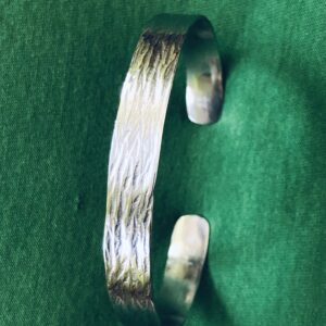 offener Armreif aus Palladium, im Muster Baumrinde von Hand geschmiedet, ca. 1 cm breit, metallisch glänzend vor dunkelgrünem Hintergrund